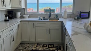 Een keuken met witte kastjes, een marmeren aanrecht, een spoelbak en uitzicht op de oceaan.
