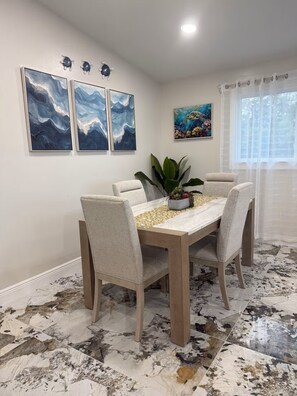 Un comedor con piso de mármol, una mesa con sillas y decoración en la pared.