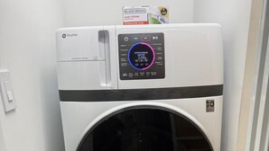Een compacte, moderne wasmachine met voorlader en een digitaal bedieningspaneel, geplaatst in een kleine wasruimte met betegelde vloer.