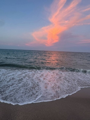 Une plage où les vagues se brisent près du rivage, avec un coucher de soleil en arrière-plan.