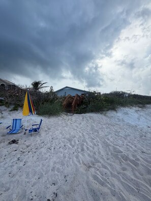 Una playa con una casa azul, una escalera de madera y un paraguas amarillo.