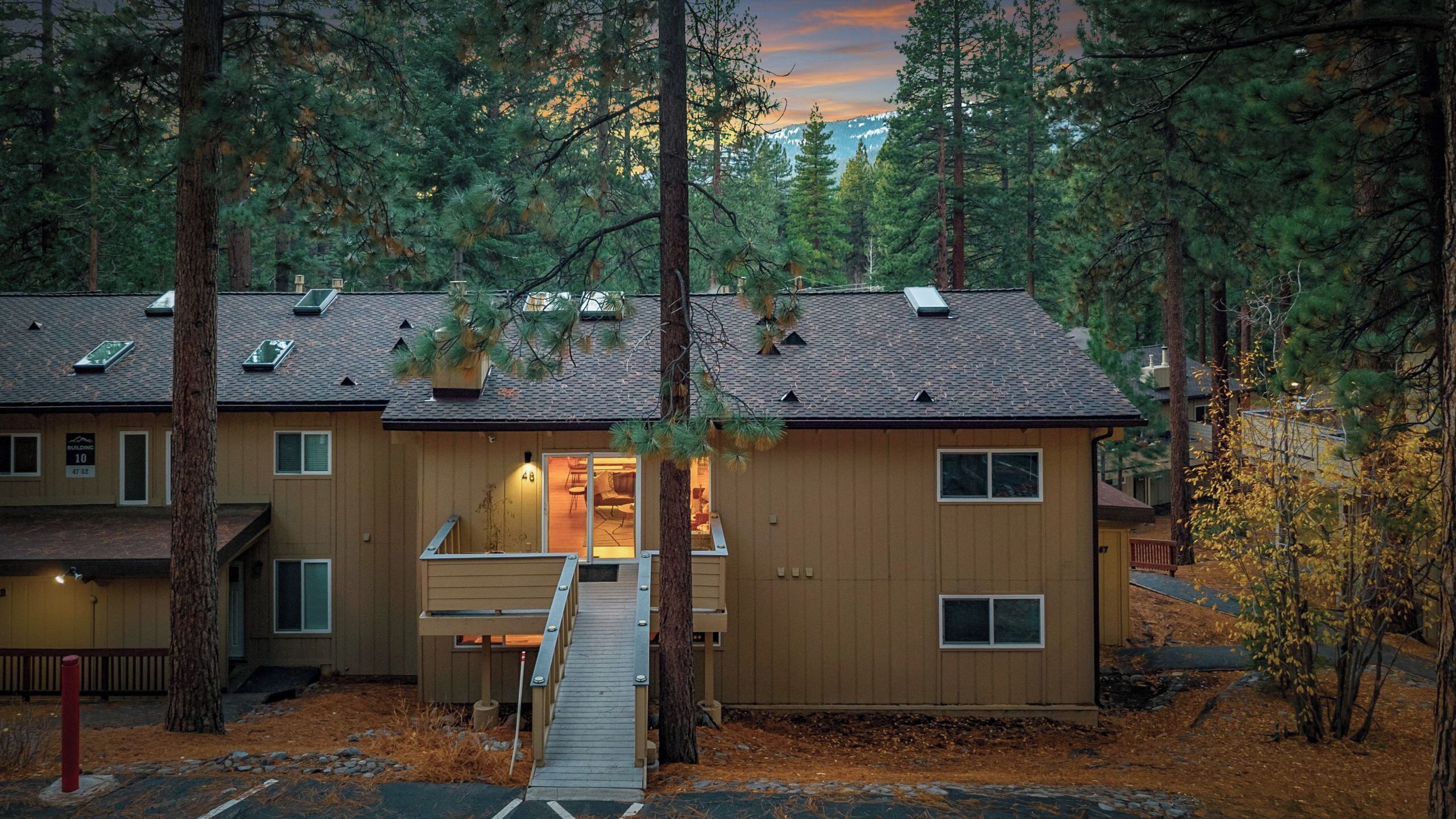 A two-story wooden cabin with a covered porch, surrounded by tall pine trees.