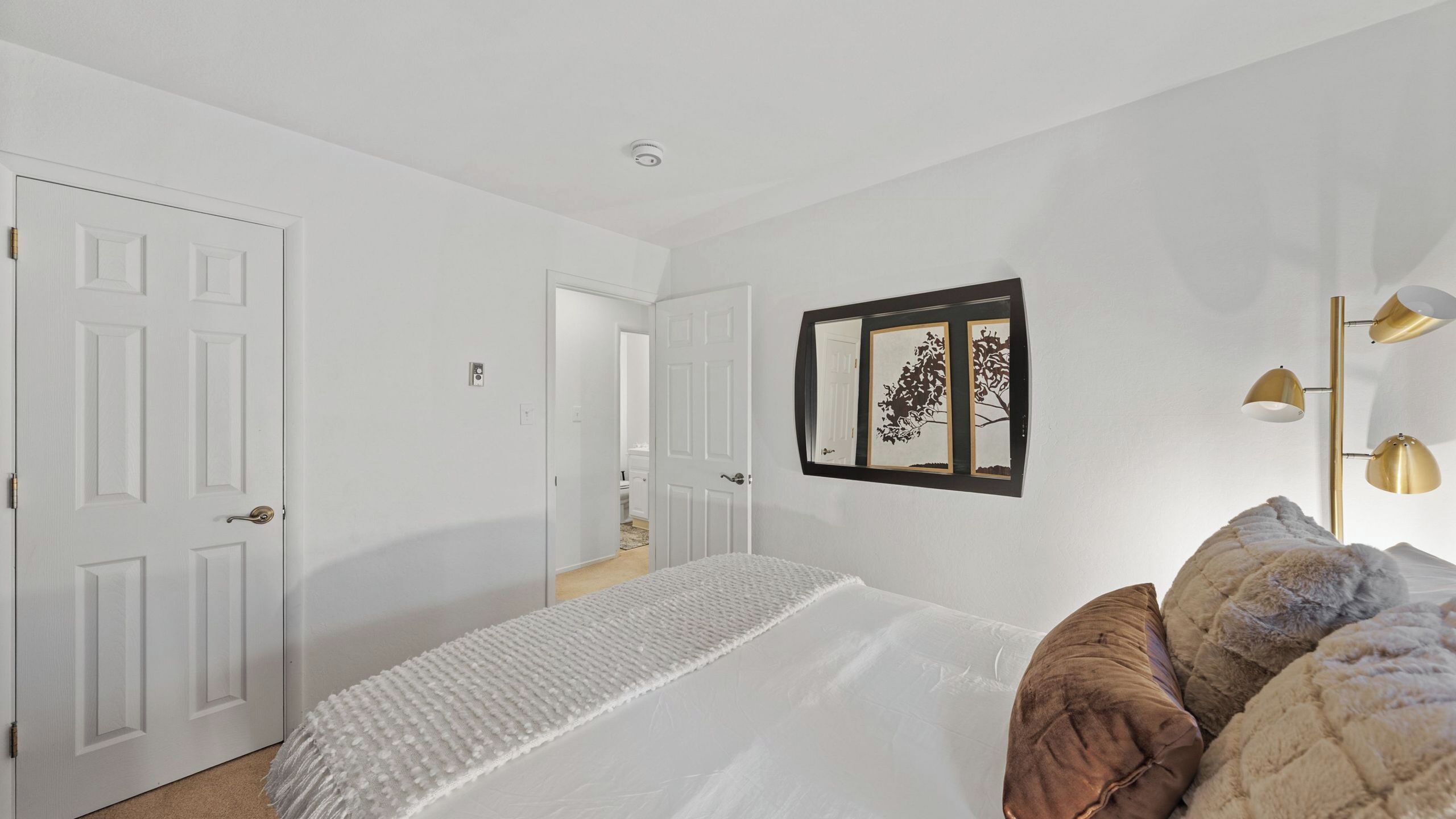 A bedroom with a bed, a wall-mounted mirror, and a bedside lamp.