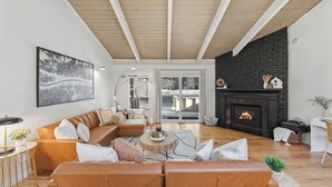 A living room with a leather sofa, a fireplace, and a large window. - Golden Mountain Chalet by Avantstay Incline Village Stay + Minutes to Lake Tahoe, Skiing + Scenic Trails (Incline Village)