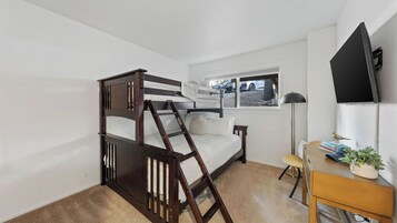 Ein Etagenbett mit einer Leiter, ein Schreibtisch mit Lampe und ein Fenster mit Blick auf einen Parkplatz.