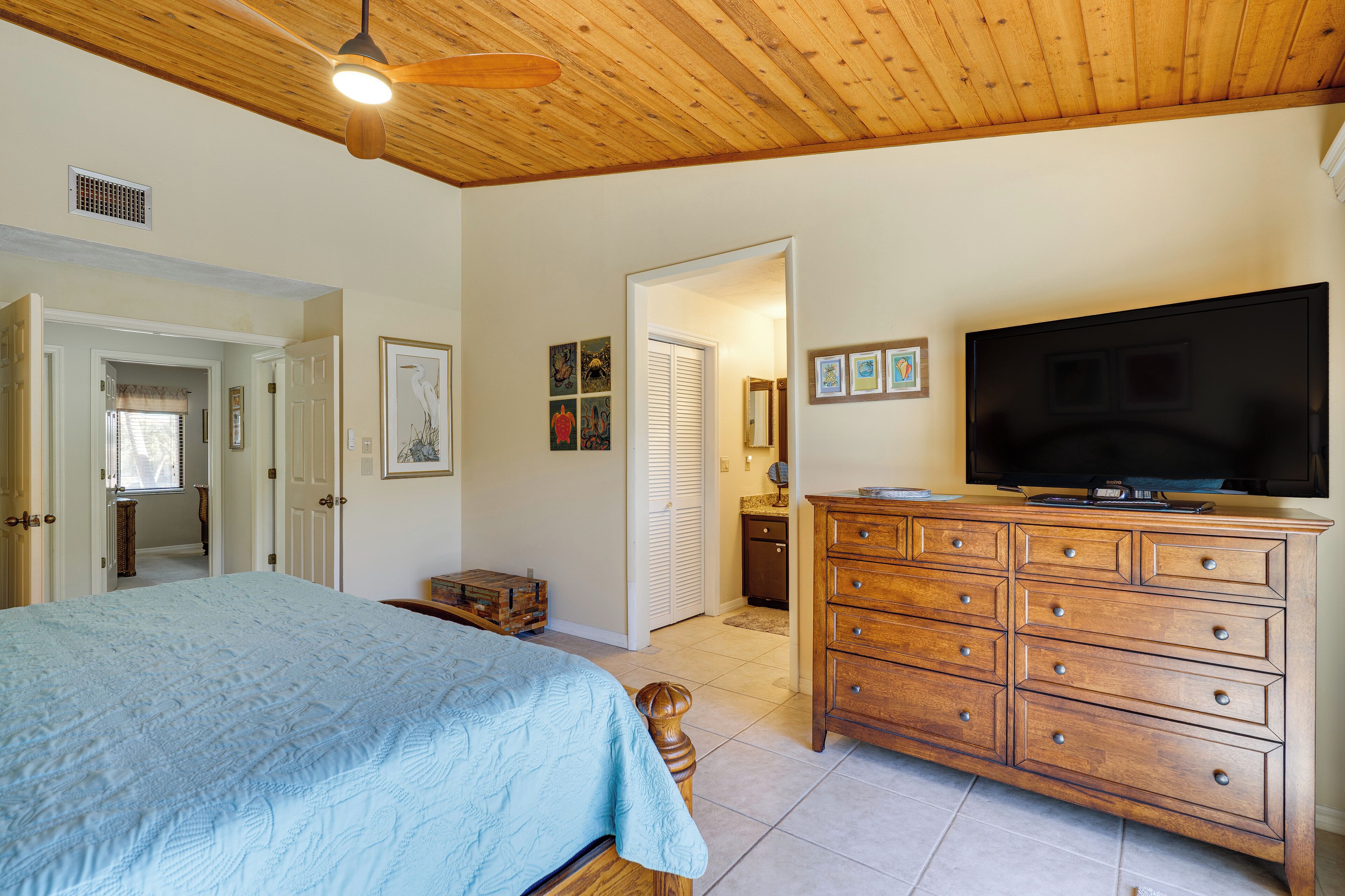 A bedroom with a bed, dresser, television, and artwork on the wall.