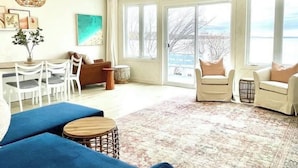 Ein großzügiges Wohnzimmer mit großem Fenster, einem blauen Sofa, einem weißen Sessel und einem Couchtisch.