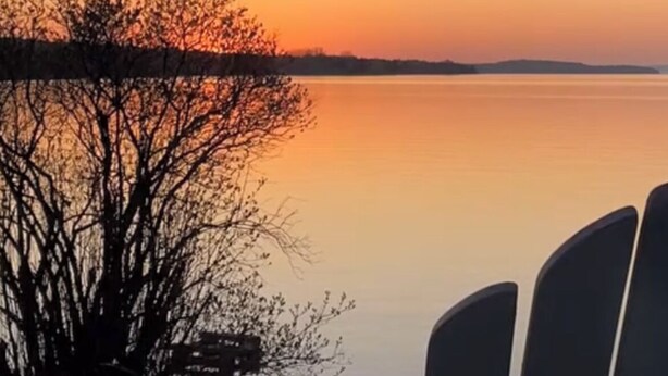 Eine Terrasse mit zwei Stühlen, die auf ruhiges Wasser bei Sonnenuntergang blicken.