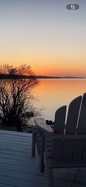 Une terrasse avec deux chaises donnant sur une étendue d’eau calme, au moment du coucher du soleil.