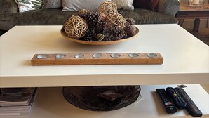 Een woonkamer met een witte salontafel, een schaal decoratieve items en een rij afstandsbedieningen.