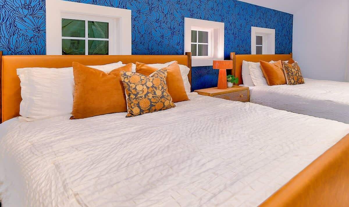 A hotel room with two beds, white bedding, and orange headboards.