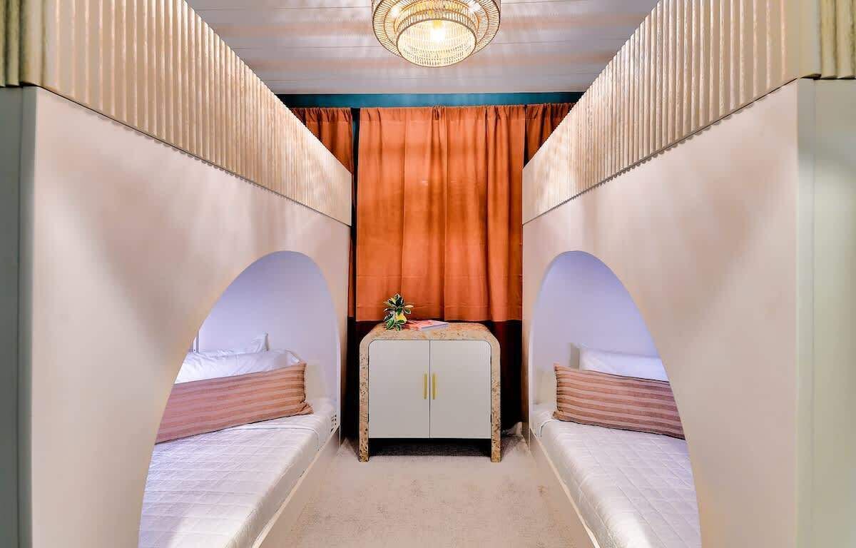 A narrow room with two beds, a central cabinet, and a chandelier.