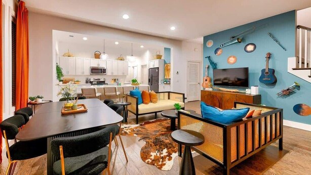 Un soggiorno moderno con zona pranzo, cucina e una parete blu decorata con strumenti musicali.