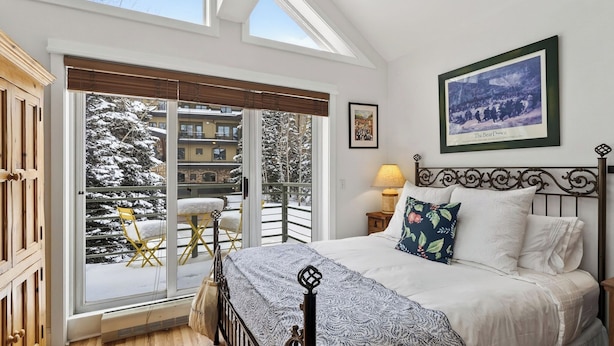 A bedroom with a bed, a nightstand, a lamp, a framed picture, and a view of a snowy balcony. - Blue Mesa Lodge 33C by Avantstay Ski-access Studio in Telluride's Mountain Village Steps From Lifts (Telluride)