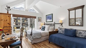 A bedroom with a bed, a sofa, a dining table with a wine glass and snacks, and a view of the outside. - Blue Mesa Lodge 33C by Avantstay Ski-access Studio in Telluride's Mountain Village Steps From Lifts (Telluride)