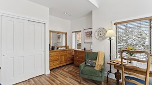 A room with a wooden floor, a green armchair, a wooden dresser, a mirror, and a window with blinds. - Blue Mesa Lodge 33C by Avantstay Ski-access Studio in Telluride's Mountain Village Steps From Lifts (Telluride)