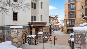 A snow-covered outdoor area with stone walls, a wooden staircase, and a sign with directional arrows. - Blue Mesa Lodge 33C by Avantstay Ski-access Studio in Telluride's Mountain Village Steps From Lifts (Telluride)