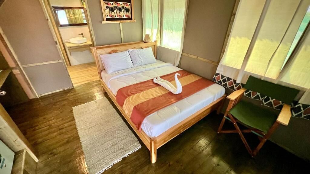 A room with a wooden bed, a green chair, a small sink, and a painting on the wall.