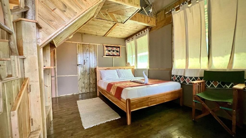 A wooden room with a bed, a chair, and a window with curtains.