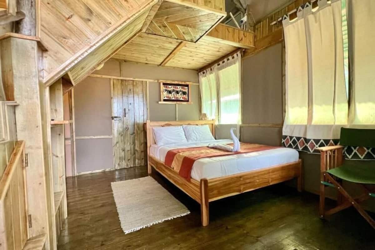 A wooden room with a bed, a chair, and a window with curtains.