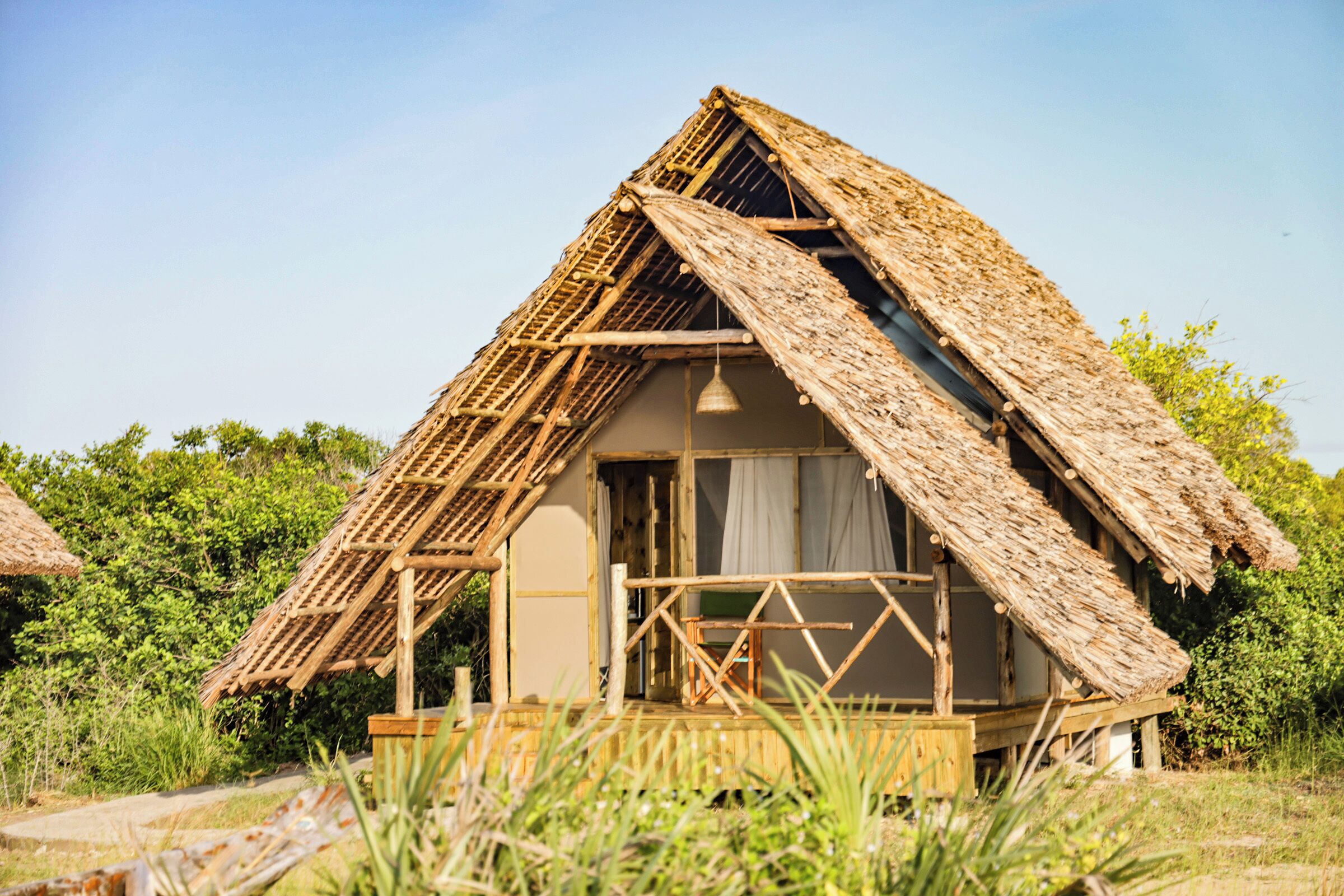 A rustic thatched-roof hut with a wooden porch and a window.