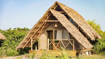 A rustic thatched-roof hut with a wooden porch and a window.