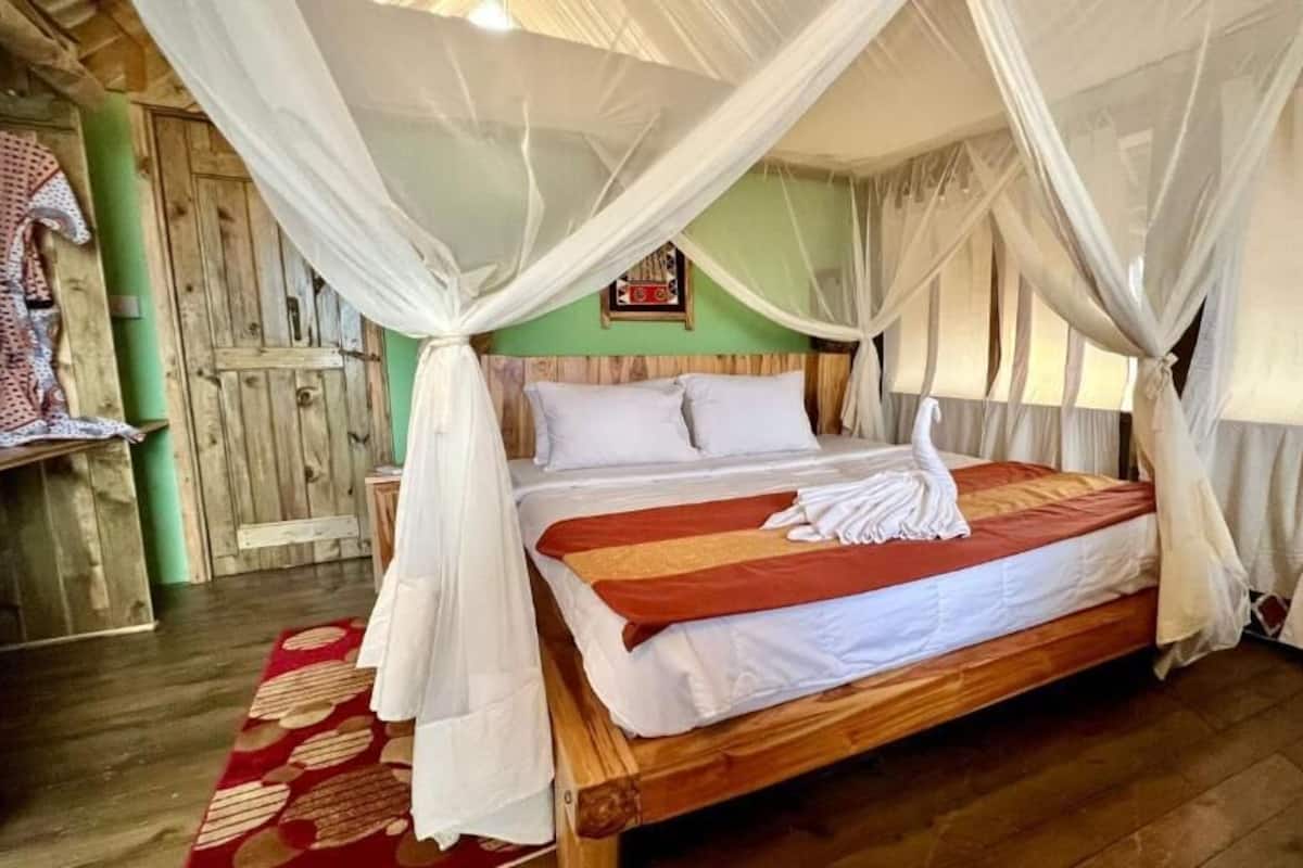 A wooden bed with white bedding, a red and white striped blanket, and a white towel.