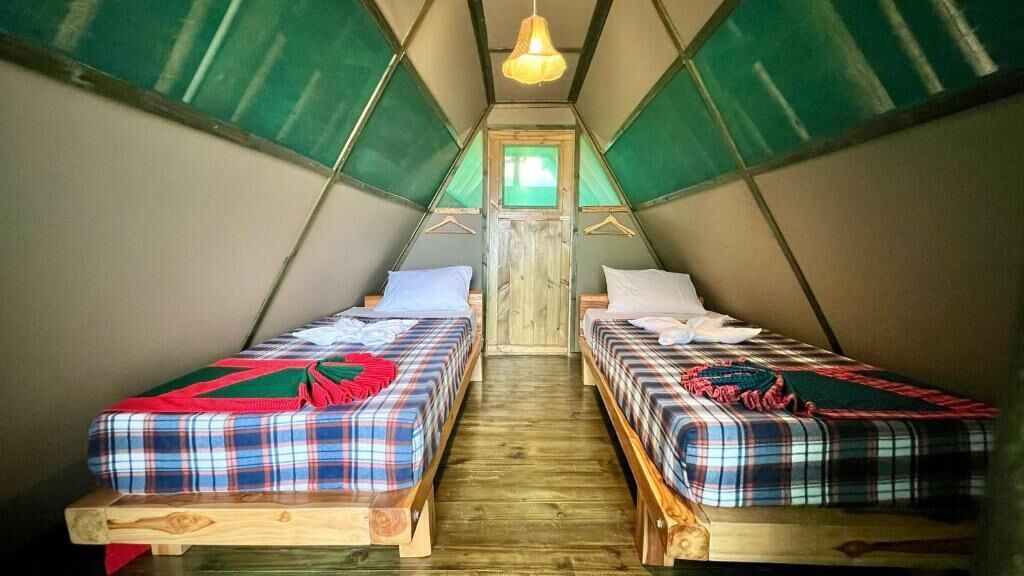Une pièce en forme de tente triangulaire, dotée de deux lits, d’un plancher en bois et d’un luminaire suspendu.