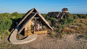 A thatched-roof hut with a wooden deck and a stone pathway leading to it.