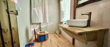 A small bathroom with a wooden floor, a white sink, a wooden chair, and a window with curtains.