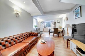 A modern living room with a leather sofa, a wooden coffee table, and a television. - Charming West Kensington Apartment • By Yoko Property (London)