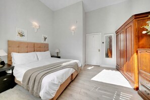 A bedroom with a large bed, bedside tables, a wardrobe, and wall-mounted lighting. - Charming West Kensington Apartment • By Yoko Property (London)