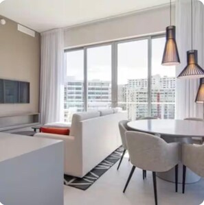 Ein modernes Hotelzimmer mit großem Fenster, einer Couch, einem Esstisch und zwei Pendelleuchten.