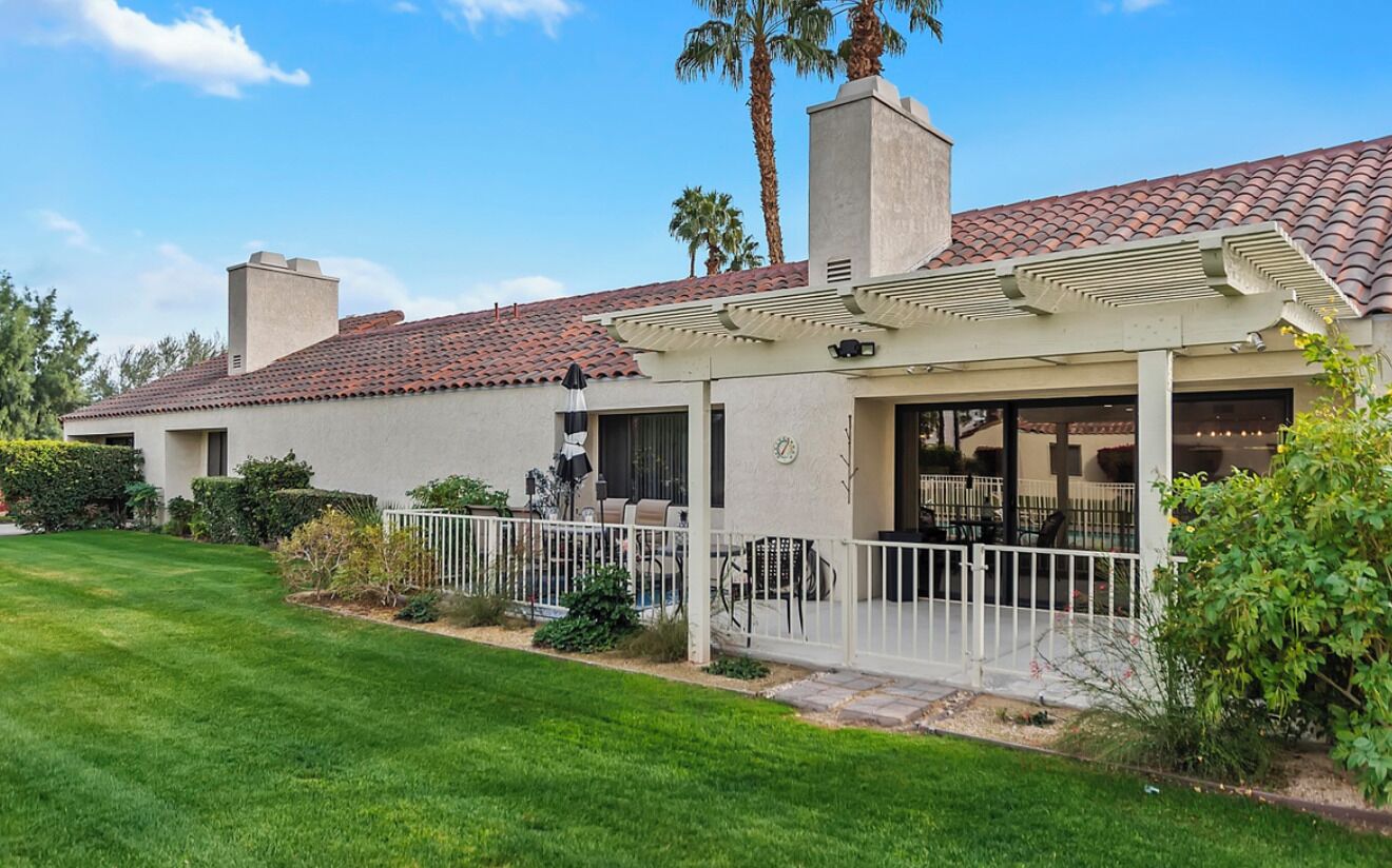 A two-story house with a covered patio, a well-maintained lawn, and a brick roof.