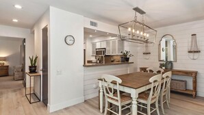 A modern kitchen with white cabinetry, a wooden dining table, and a chandelier. - STUNNING FURNISHED POOLSIDE HOME AT MISSION HILLS COUNTRY CLUB RANCHO MIRAGE (Rancho Mirage)