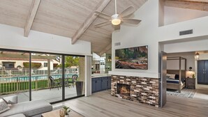 A spacious living area with a fireplace, a ceiling fan, and a view of a swimming pool. - STUNNING FURNISHED POOLSIDE HOME AT MISSION HILLS COUNTRY CLUB RANCHO MIRAGE (Rancho Mirage)
