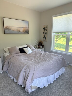 A bedroom with a large bed, a nightstand, a window with blinds, and a painting on the wall. - A Private Retreat Near Road America, Walk to Downtown Elkhart Lake, Sleeps 12 (Elkhart Lake)