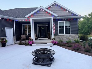 A house with a covered porch, a welcome sign, an American flag, and a fire pit in the front yard. - A Private Retreat Near Road America, Walk to Downtown Elkhart Lake, Sleeps 12 (Elkhart Lake)