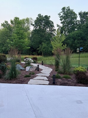 A stone pathway leading through a landscaped garden with trees and a bird feeder. - A Private Retreat Near Road America, Walk to Downtown Elkhart Lake, Sleeps 12 (Elkhart Lake)