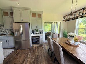 A kitchen with a stainless steel refrigerator, wooden dining table, and chairs. - A Private Retreat Near Road America, Walk to Downtown Elkhart Lake, Sleeps 12 (Elkhart Lake)