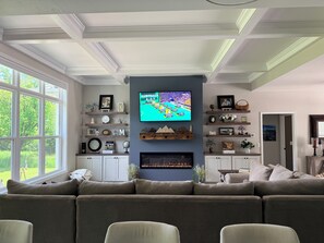 A living room with a large television, a fireplace, and a view of the outdoors. - A Private Retreat Near Road America, Walk to Downtown Elkhart Lake, Sleeps 12 (Elkhart Lake)