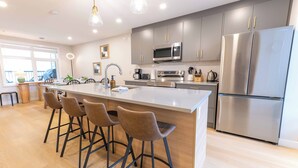 A modern kitchen with a central island, bar stools, stainless steel appliances, and a large refrigerator.