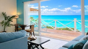 Ein Zimmer mit Holzboden, Deckenventilator, großem Fenster mit Meerblick, Sofa, Tisch und Stuhl.