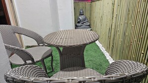 Mobili in vimini con un tavolo rotondo e sedie, una statua di Buddha e una recinzione in bambù.