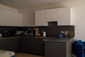 Une cuisine moderne avec des meubles de rangement de couleur sombre, un four à micro-ondes, un évier et une machine à café.