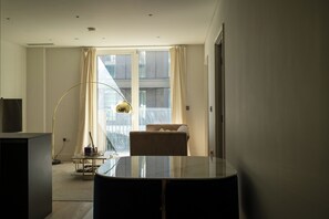 A modern hotel room with a large window, a round table, a sofa, and a floor lamp. - Stylish New-Build Flat for 2 in Battersea (London)
