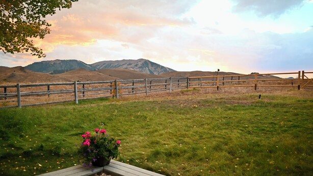 A wooden bench with a flower pot, a grassy field, and a wooden fence with mountains in the background. - Private 4 Bedroom 4 Bath Sun Valley Getaway. Hot Tub/Large Yard/ Dog Friendly (Sun Valley)