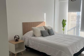 Ein modernes Schlafzimmer mit einem hölzernen Kopfteil, einer weißen Bettdecke und einem kleinen Nachttisch mit Lampe.