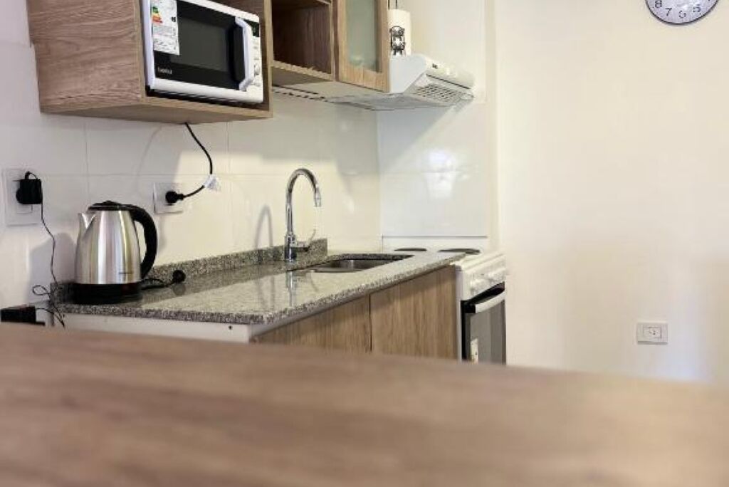 Una cucina con forno a microonde, bollitore, lavandino e pensili in legno.