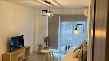 Ein modernes Wohnzimmer mit Flachbildfernseher, einer Couch, einem Couchtisch und einem großen Fenster mit Aussicht.
